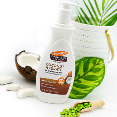 Palmer's Coconut Oil Formula Coconut Hydrate Body Lotion, the best moisturizer for all skin types, on table with coconut pieces and green coffee beans