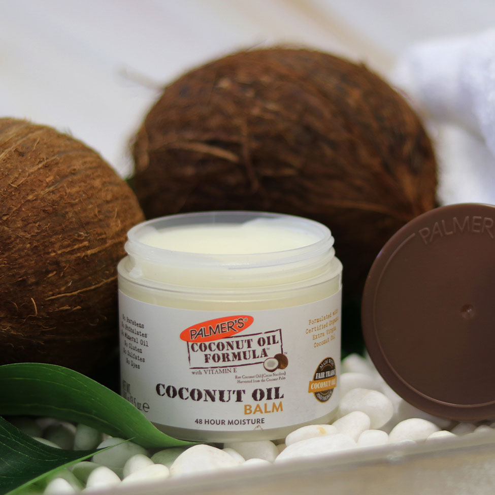 Palmer's Coconut Oil Balm, a solid coconut oil for feet product, on a table with coconuts