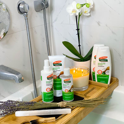 Palmer's Coconut Oil Formula hair care collection, ideal for taking care of wavy hair, on a bath tray with a candle lit