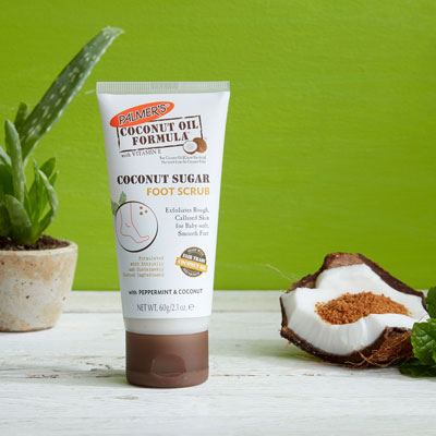 A winter foot care staple, Palmer's Coconut Oil Formula Coconut Sugar Foot Scrub on a table with coconut piece and sugar