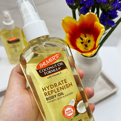 Palmer's Coconut Hydrate Body Oil, the best body oil for glowing skin, held in hand above flowers