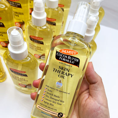 Palmer's Skin Therapy Oil, one of the best body oils for glowing skin, held in hand over other body oils