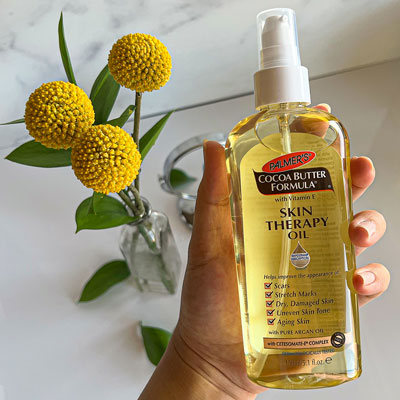 Palmer's Skin Therapy Oil, one of the best oils for skin repair, held in woman's hand with flowers in the background