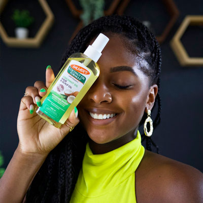 Smiling Black woman with box braids with curls holding a Palmer's Coconut Oil Hair & Scalp Oil 