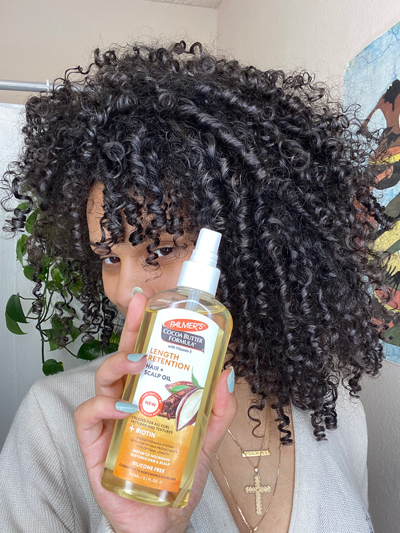 Palmer's Cocoa Butter Formula Length Retention Hair Oil for low porosity hair held by black woman with curly hair.