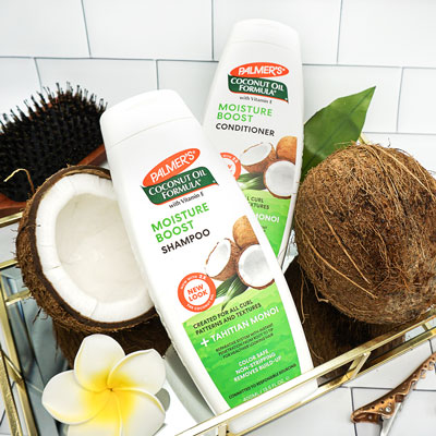 Palmer's Coconut Oil Formula Moisture Boost Shampoo and Conditioner for heat-damaged curls on bathroom counter with coconuts
