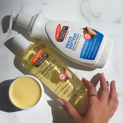 Palmer's Cocoa Butter skin care, perfect for healing dry skin, on marble counter with woman's hand reaching for it