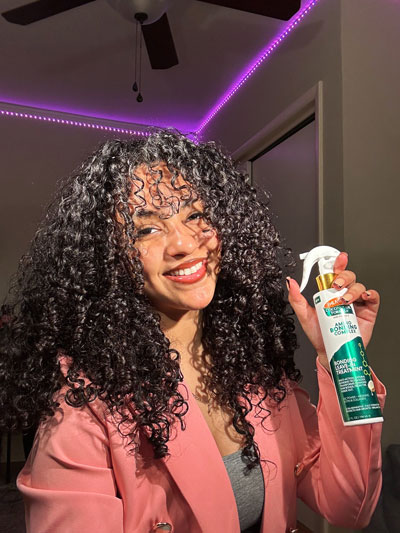 Black woman with curls holding Palmer's Leave-In Treatment, one of the best leave-in conditioners