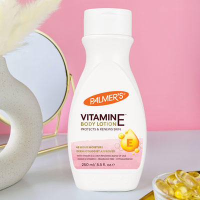 Palmer's Vitamin E for dry skin lotion on a table with vitamin e capsules, mirror and vase