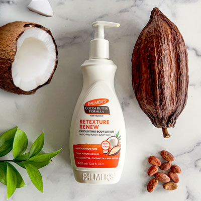 Palmer's Cocoa Butter Formula Retexture Renew Body Exfoliating Body Lotion, ideal for strawberry skin, on table with ingredients