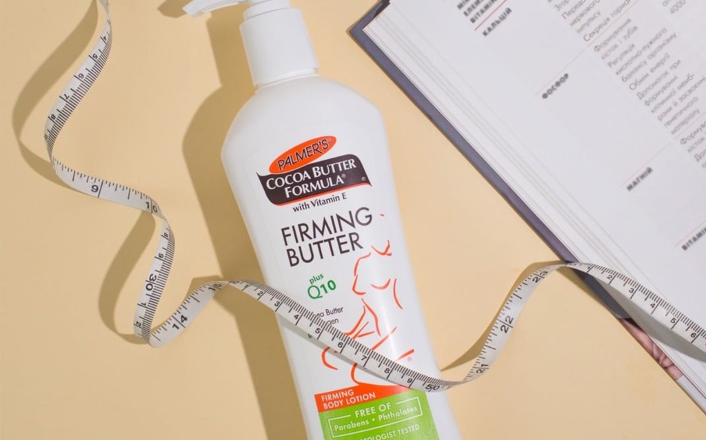 Palmer's Cocoa Butter Formula Firming Butter, the best tummy firming cream after pregnancy, on table with measuring tape and book
