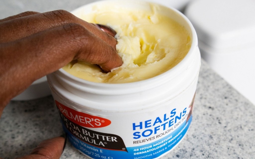 Black woman dipping her fingers into the Palmer's Cocoa Butter Jar for one of the many cocoa butter uses and beauty hacks