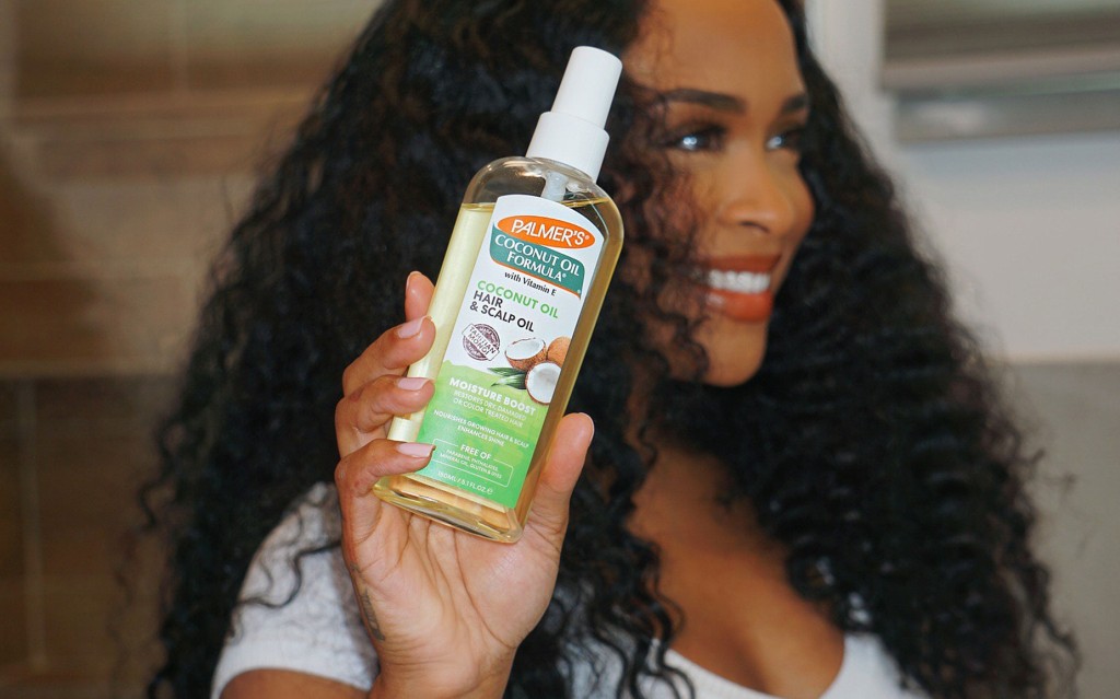 Black woman holding Palmer's Coconut Oil for Hair & Scalp Oil while smiling