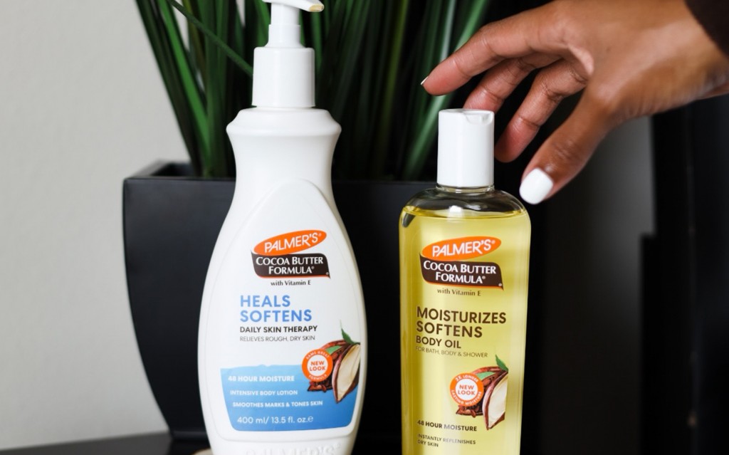 Palmer's Cocoa Butter Formula Body Lotion and Oil for fall skin care on table with hand reaching to pick up