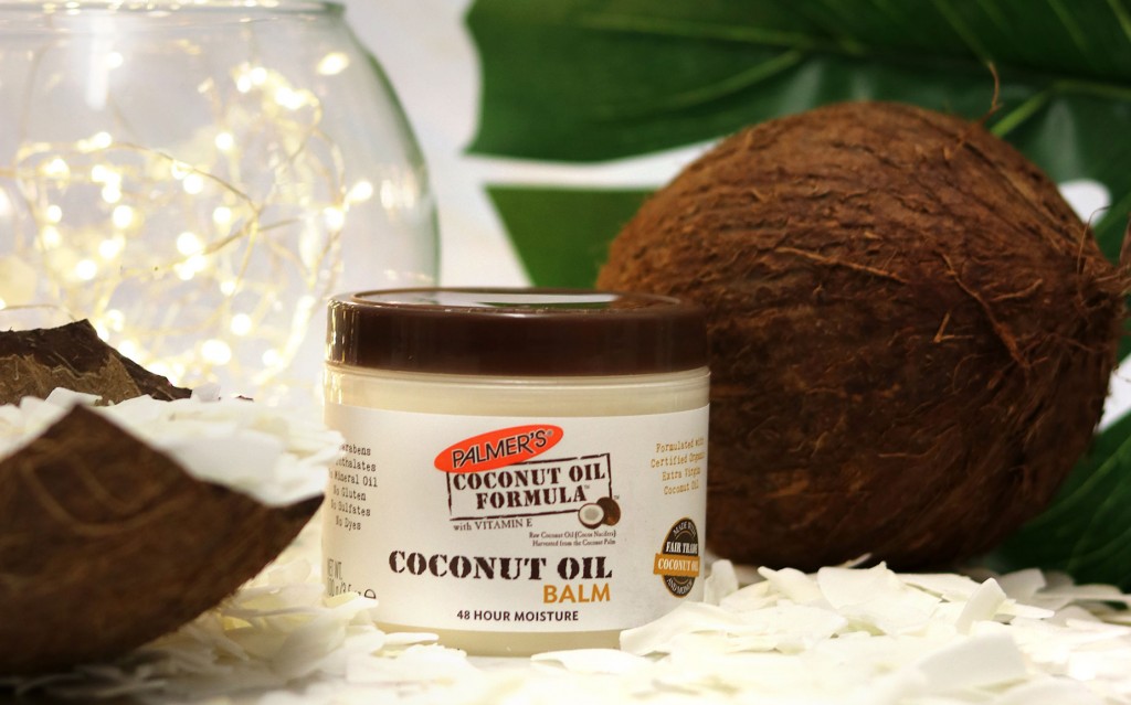 Palmer's Coconut Oil Balm, a dry skin balm, on a table with coconuts and coconut flakes