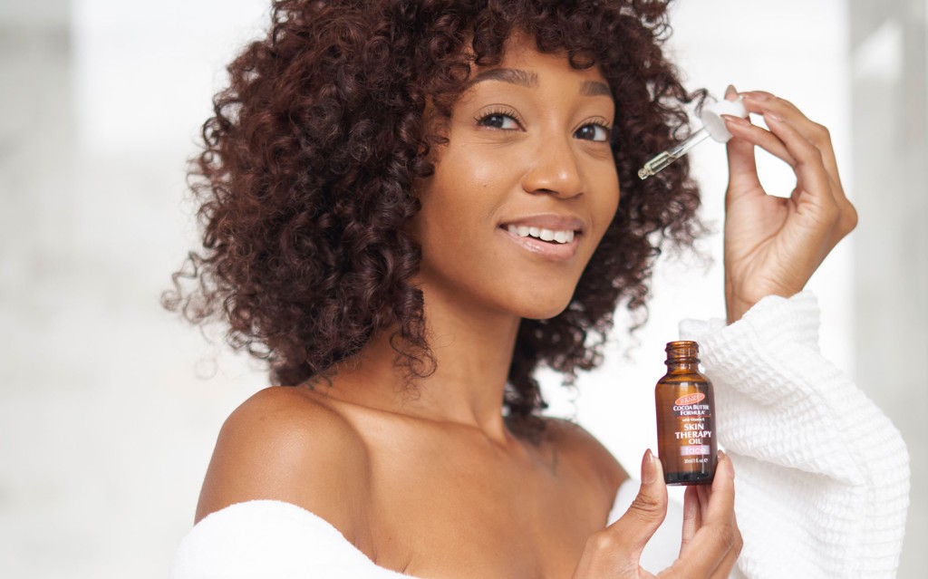 A Black woman applying Palmer's Skin Therapy Face Oil, a key skin cycling product, as part of her skin cycling routine