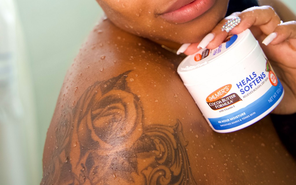 Black woman with tattoo holding Palmer's Cocoa Butter Formula Original Solid Jar, part of her tattoo aftercare routine