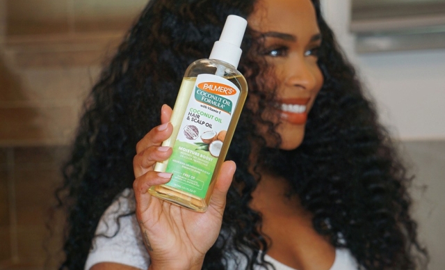 Black woman holding Palmer's Coconut Oil for Hair & Scalp Oil while smiling