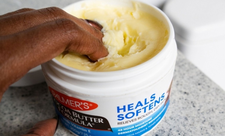 Black woman dipping her fingers into the Palmer's Cocoa Butter Jar for one of the many cocoa butter uses and beauty hacks