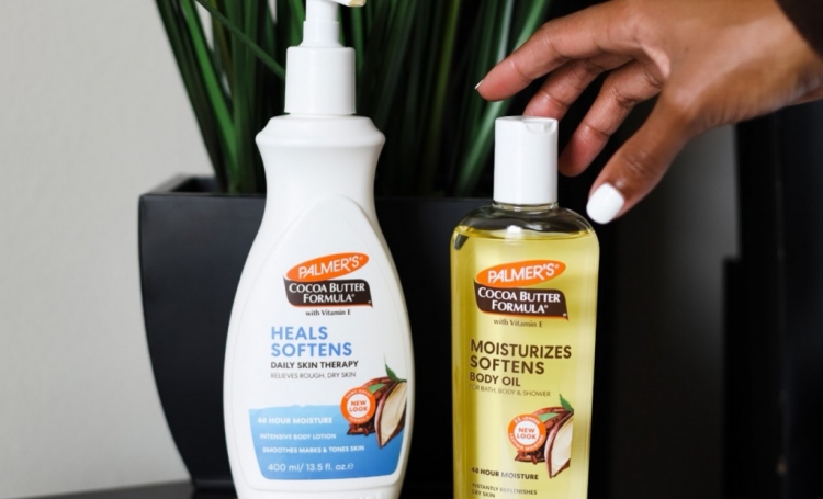 Palmer's Cocoa Butter Formula Body Lotion and Oil for fall skin care on table with hand reaching to pick up