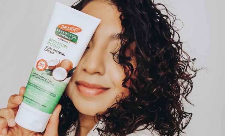 Curly haired woman holding Palmer's Coconut Oil Formula Curl Defining Cream for Heat-Damaged Curls