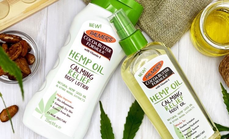 Palmer's Hemp Oil Body Lotion & Body Oil on table to cocoa beans and hemp oil and leaves