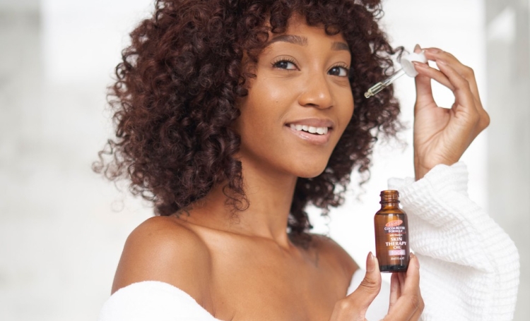 A Black woman applying Palmer's Skin Therapy Face Oil, a key skin cycling product, as part of her skin cycling routine
