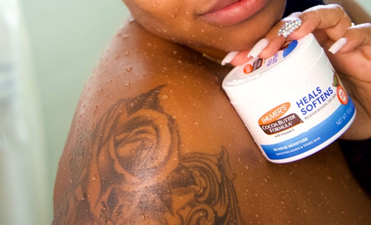 Black woman with tattoo holding Palmer's Cocoa Butter Formula Original Solid Jar, part of her tattoo aftercare routine
