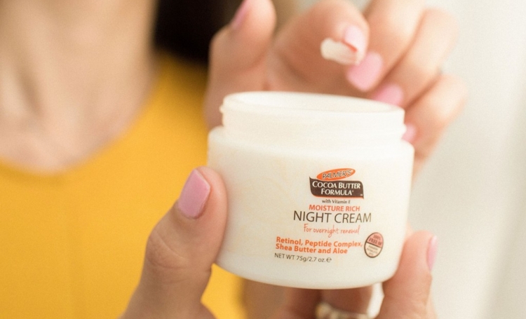 Palmer's Cocoa Butter Formula Night Renewal Cream, an essential in the best nighttime skin care routines, in hand with cream on finger